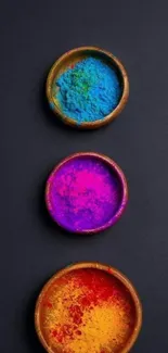 Three bowls of vibrant colored powder on a black background.