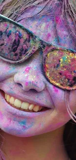 A smiling face covered in colorful Holi powders with vibrant sunglasses.