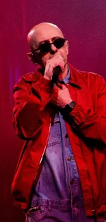 Performer in red jacket singing under vibrant stage lights.