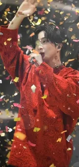 Singer in red shirt performing amid colorful confetti.