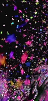 Vibrant confetti against a black background with raised hands.