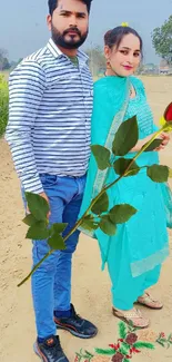 Couple in a rural setting holding a rose with lush fields in the background.