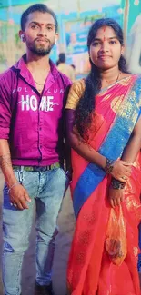 Traditional couple in vibrant attire at a cultural festival with colorful decor.