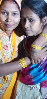 Two women in traditional vibrant attire embracing each other joyfully.