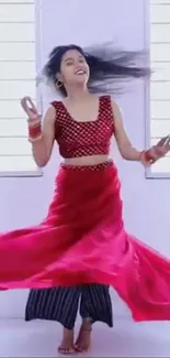 Woman dancing gracefully in vibrant red attire indoors.