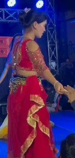 Dancer in vibrant red costume performs on stage with colorful lights.