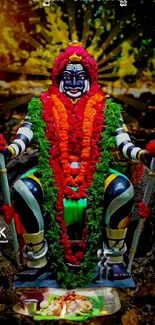 Vibrant deity with red and green garlands on a mobile wallpaper.