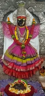 Intricate deity statue adorned with vibrant colors and floral offerings in a temple.