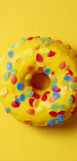 Yellow donut with colorful sprinkles on a yellow background.