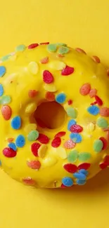 Yellow frosted donut with colorful sprinkles on a matching background.