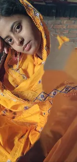 Woman in vibrant orange traditional attire with brick backdrop.