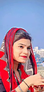 Portrait of woman with vibrant red and black ethnic attire against city backdrop.