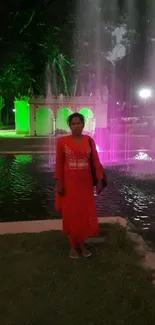 Woman standing by a fountain with colorful night lights in a serene evening setting.