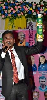 Enthusiastic speaker at colorful event with floral backdrop.