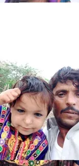 Father and child in colorful attire with natural backdrop.