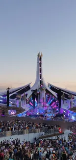 Festival stage with colorful lights at sunset, crowd in foreground.