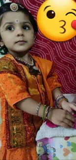 Child in orange dress with festive decor and emojis.