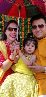 Family celebrating under colorful umbrella in festive attire.