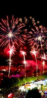 Fireworks burst over a vibrant cityscape at night.