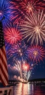 Colorful fireworks burst over a lake with an American flag.