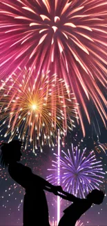 Silhouette dance beneath vibrant fireworks in night sky.