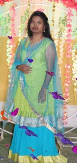 Woman in traditional turquoise attire with vibrant floral backdrop.