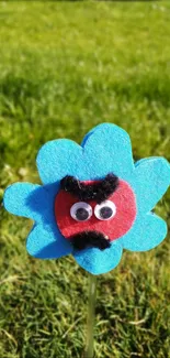 Vibrant felt cartoon flower on lush grass background.