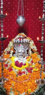 Floral deity sculpture with vibrant flowers and candles.