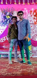 Two men posing at a colorful floral event with vibrant decorations.