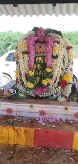 Floral-decorated deity in Indian temple setting, vibrant and colorful.