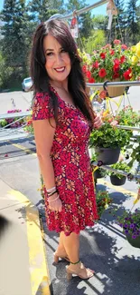 Woman standing in a vibrant flower garden wearing a red patterned dress.