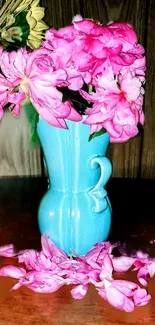 Blue vase with pink flowers and scattered petals on wooden table.