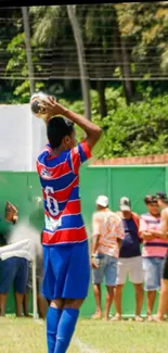 Player in blue and red jersey taking a throw-in on a green football field.