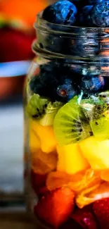 Colorful layered fruit in a glass jar, perfect for a vibrant wallpaper.