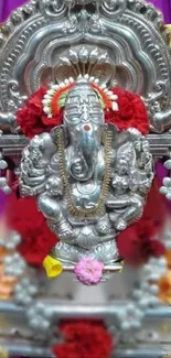 Ganesh idol with silver and floral decor on a vibrant background.