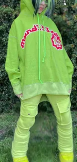 Person in a vibrant green hoodie standing against a lush background.