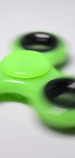 Close-up of a vibrant green fidget spinner with black rings on a soft focus background.