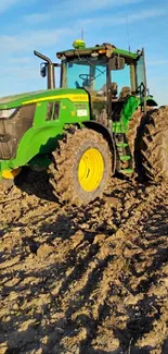 Green tractor in a plowed field under bright blue sky.