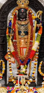 Hindu deity adorned with colorful garlands and ornate jewelry in temple setting.