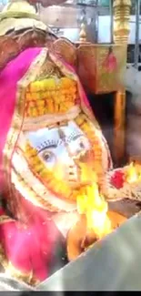 Hindu deity adorned with flowers and flames in a temple setting.