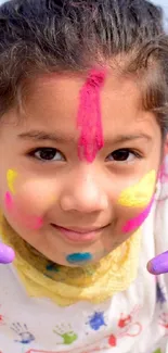 Child with colorful face paint and joyful expression celebrating Holi.