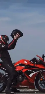 Rider holding helmet on red Honda motorcycle, scenic view.