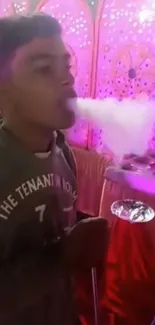 Man exhaling hookah smoke against a pink backdrop.