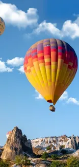 Colorful hot air balloons floating over rocky landscape and blue sky.