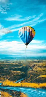 Vibrant hot air balloon soaring over scenic landscape under a clear blue sky.