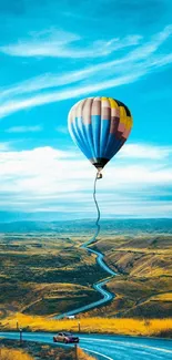 Hot air balloon over a winding road landscape with blue skies.