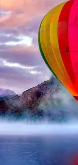 Vibrant hot air balloon over misty landscape and calm water.