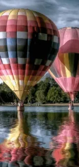 Vibrant hot air balloons reflecting on serene lake against blue sky backdrop.