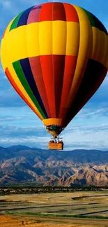 Colorful hot air balloon above mountains and blue sky.