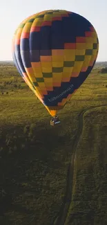 Colorful hot air balloon over green landscape.